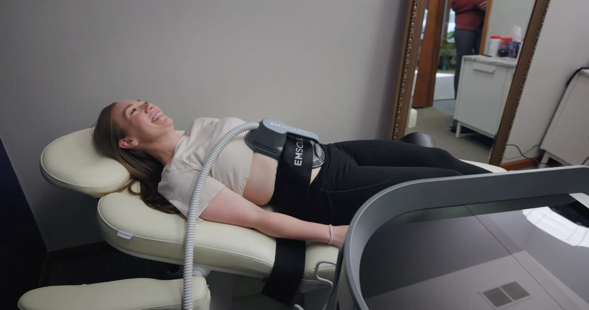 A patient relaxing during an EMSCULPT NEO session, the applicator strapped across her abdomen